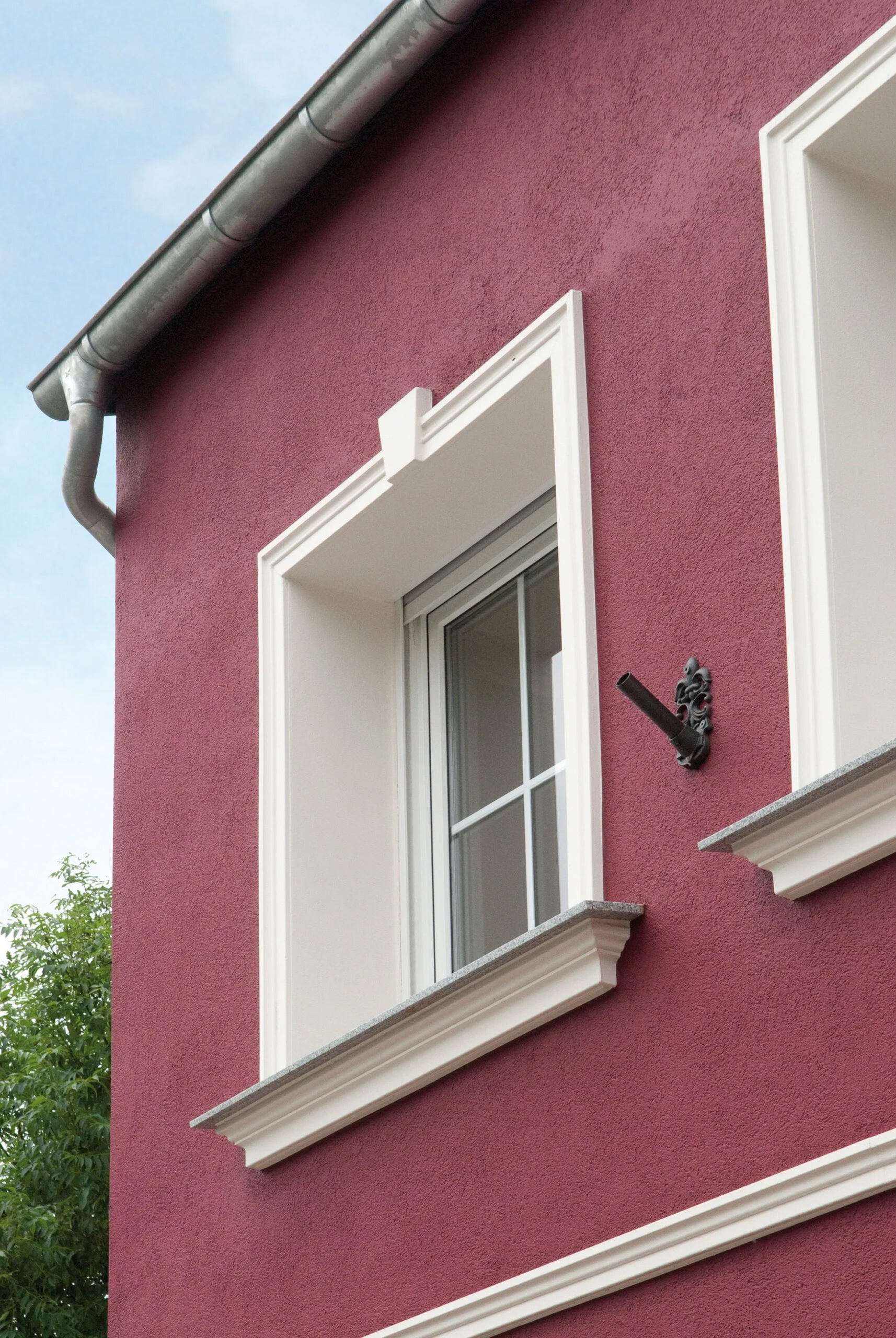 Moldura decorativa blanca para ventana en fachada exterior color burdeos, estilo clásico.