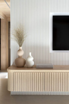 Mueble moderno de listones de madera frente a pared con moldura decorativa blanca y jarrones minimalistas.