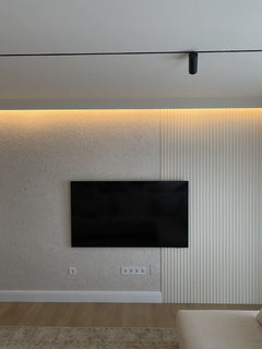 Pared con moldura decorativa, panel acanalado y televisor en sala moderna, iluminación LED.