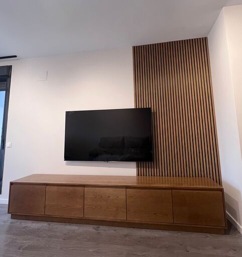 Salón moderno con panel decorativo de madera, mueble bajo y pared blanca, TV montada.