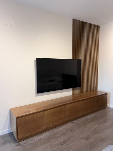 Mueble bajo de madera con panel decorativo de listones y televisor en pared moderna