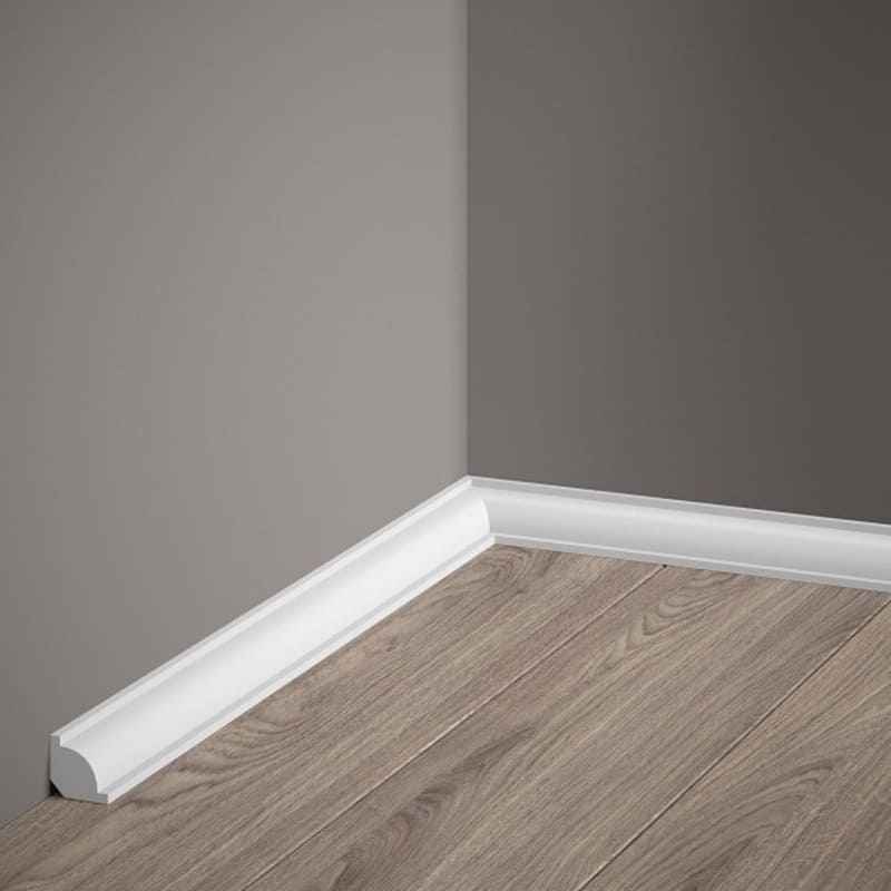 Rodapié blanco decorativo en esquina de pared gris y suelo laminado imitación madera.