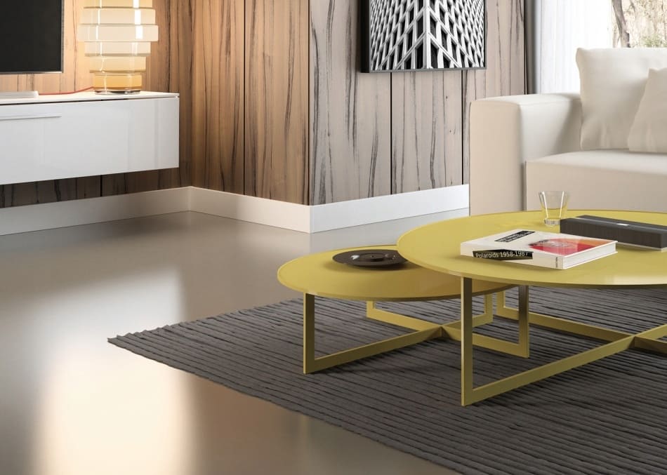 Salón moderno con rodapié blanco, suelo gris, mesa baja amarilla y pared decorativa de madera.