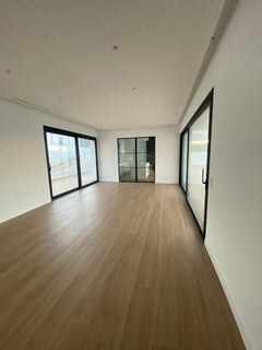 Salón moderno con suelo de madera, paredes blancas y grandes ventanales de aluminio negro.