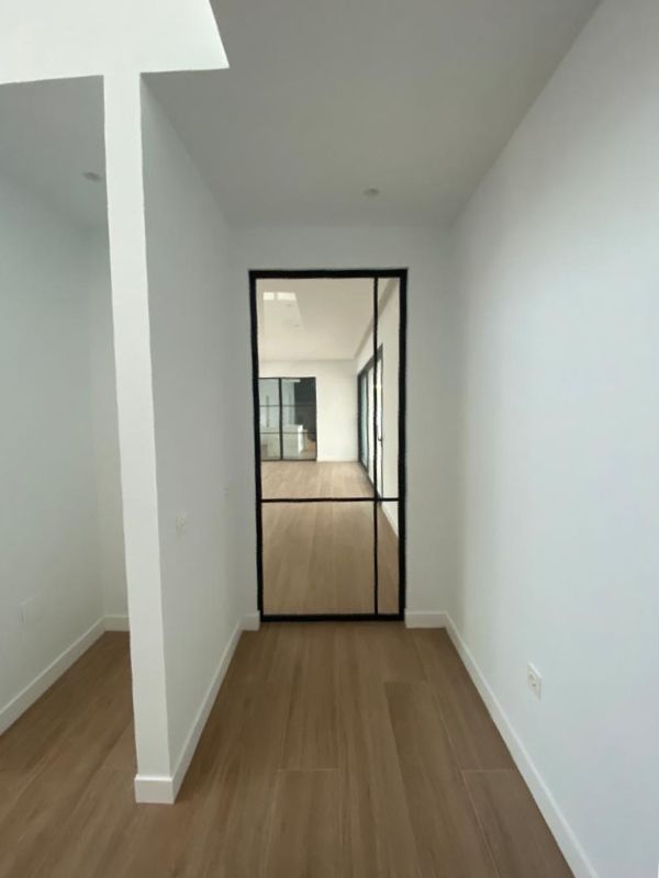 Pasillo moderno con suelo de madera, paredes blancas y puerta de vidrio negro.
