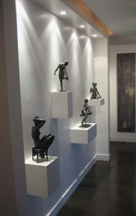 Esculturas decorativas sobre pedestales blancos en pared iluminada de pasillo moderno.