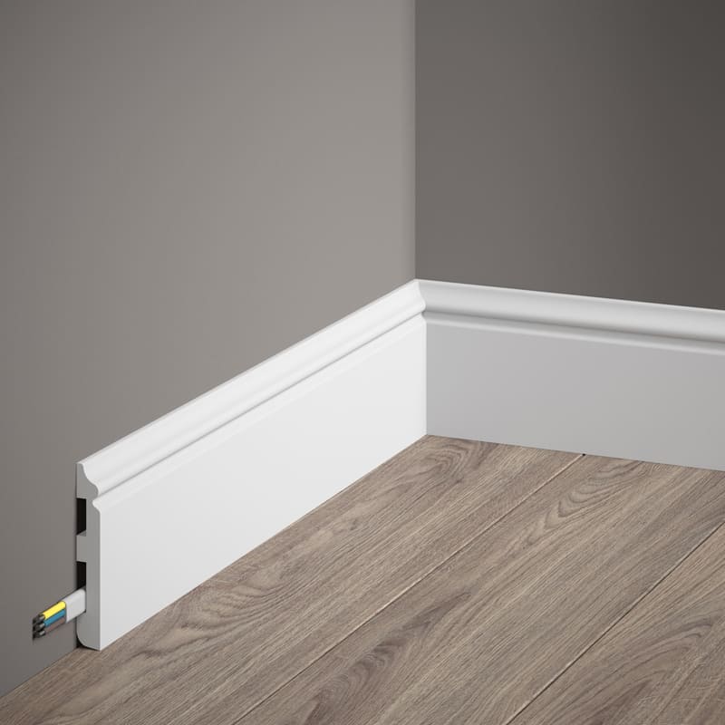 Rodapié blanco decorativo con canaleta para cables en esquina de pared gris y suelo madera.
