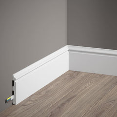 Rodapié blanco decorativo con canaleta para cables en esquina de pared gris y suelo madera.
