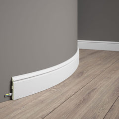 Rodapié blanco flexible instalado en pared curva con suelo laminado madera.