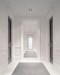 Pasillo elegante con rodapié blanco de PVC, molduras decorativas y puertas oscuras.