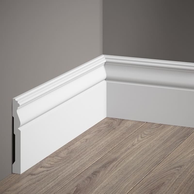 Rodapié decorativo blanco con moldura clásica en pared gris y suelo de madera.