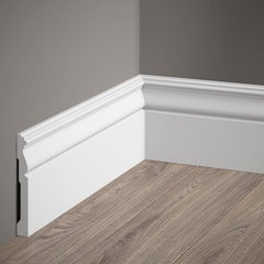 Rodapié decorativo blanco con moldura clásica en pared gris y suelo de madera.