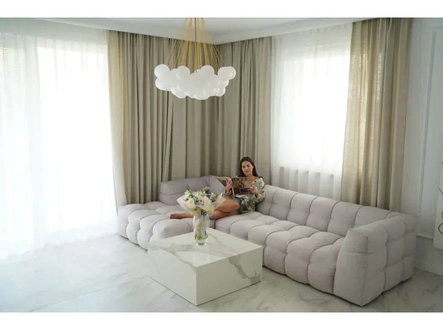 Sala moderna con sofá esquinero tapizado, mesa de centro blanca y cortinas elegantes