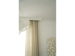 Moldura decorativa blanca en techo, cortina beige y pared blanca con arte dorado.