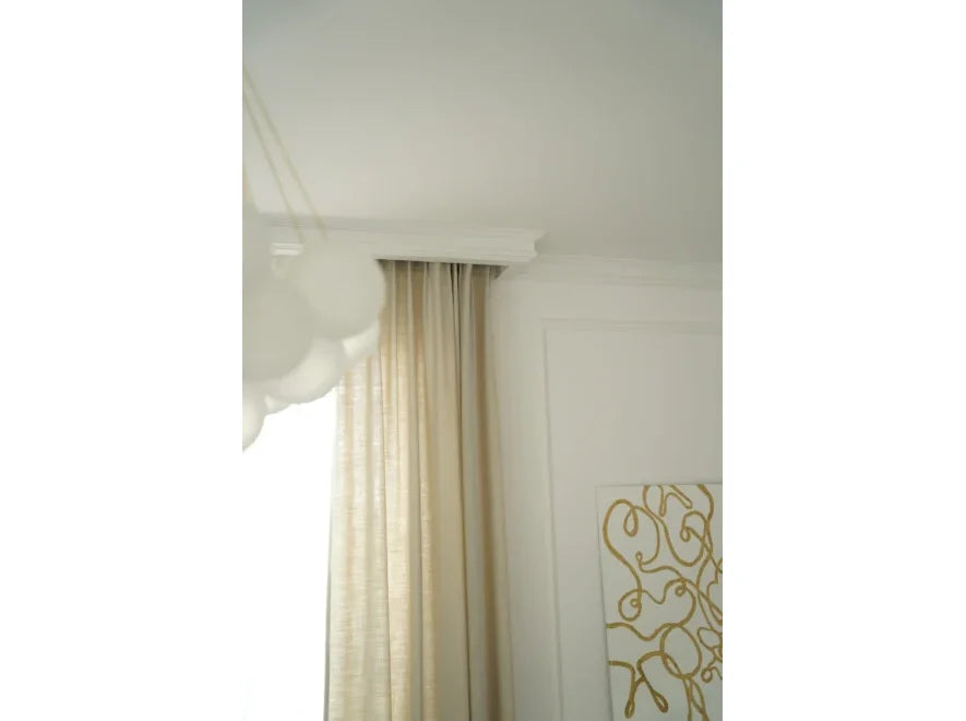 Moldura decorativa blanca en techo, cortina beige y pared blanca con arte dorado.