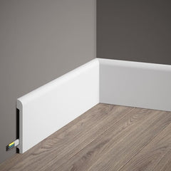 Rodapié blanco moderno con canaleta para cables en esquina de pared gris y suelo de madera clara.