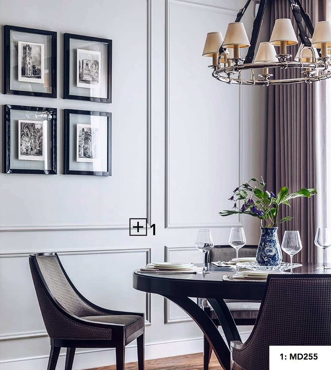 Comedor elegante con molduras decorativas en pared, mesa redonda y cuadros enmarcados.