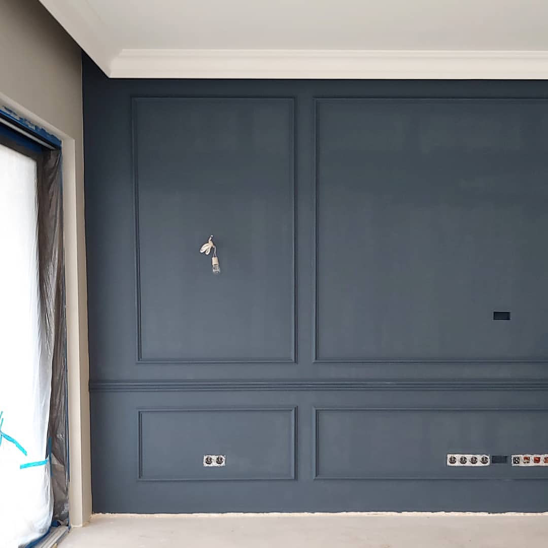 Pared azul oscuro con molduras decorativas y rodapiés blancos en interior moderno
