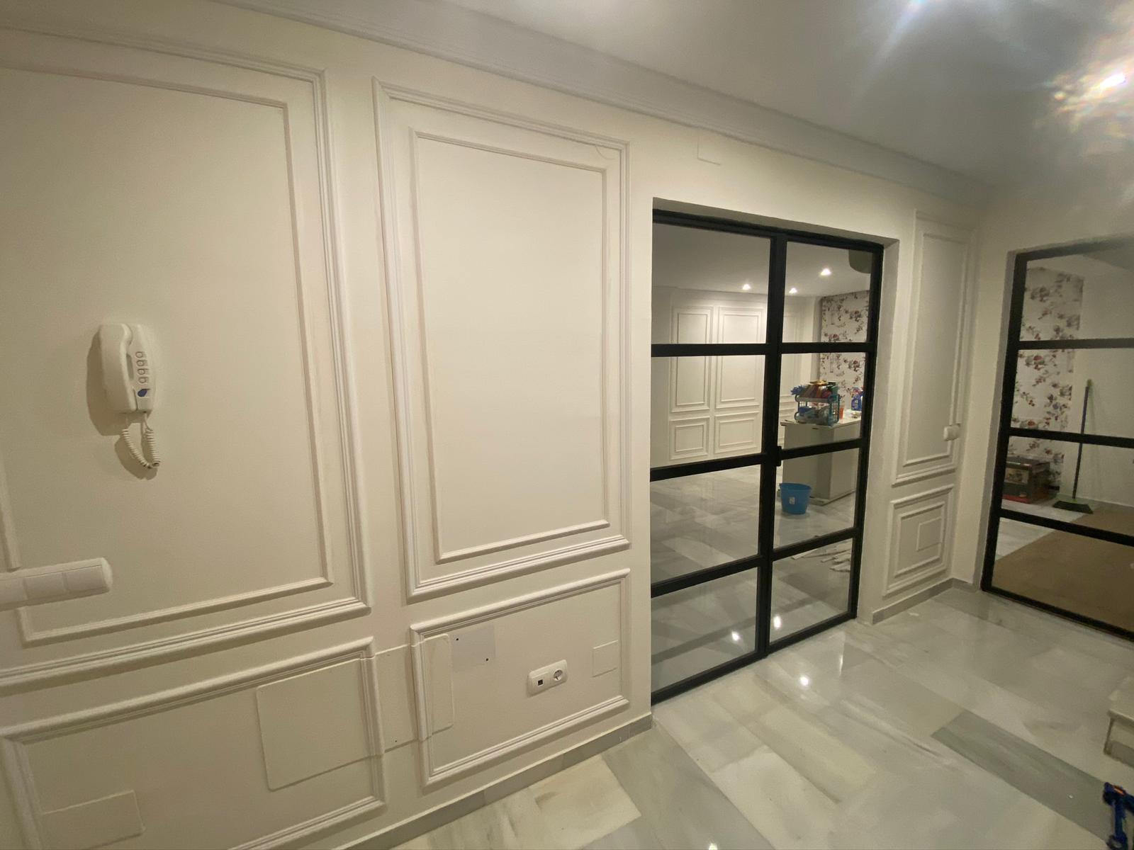 Pared interior decorada con molduras blancas y puertas de vidrio con marco negro