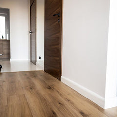 Rodapié blanco decorativo en pasillo con suelo de madera y puertas de madera oscura