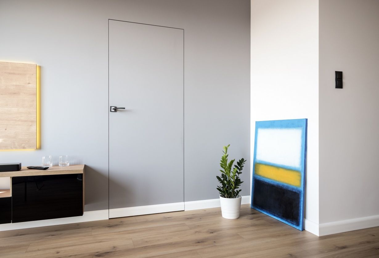 Puerta lisa gris con moldura decorativa, rodapié blanco y suelo de madera clara en interior moderno.