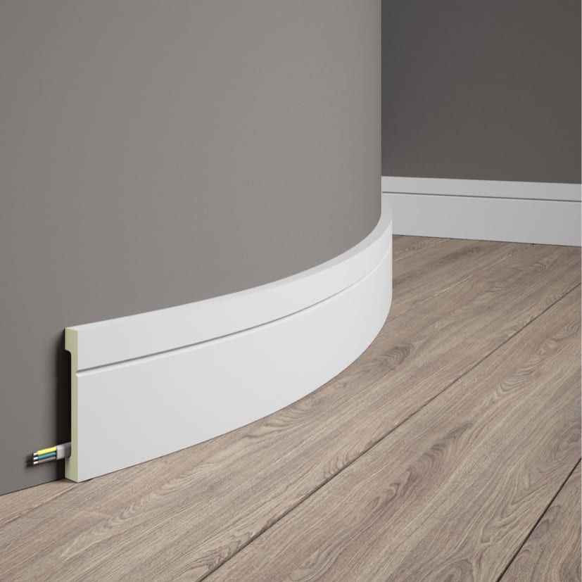 Rodapié flexible blanco instalado en pared curva y suelo de madera, cubre cables