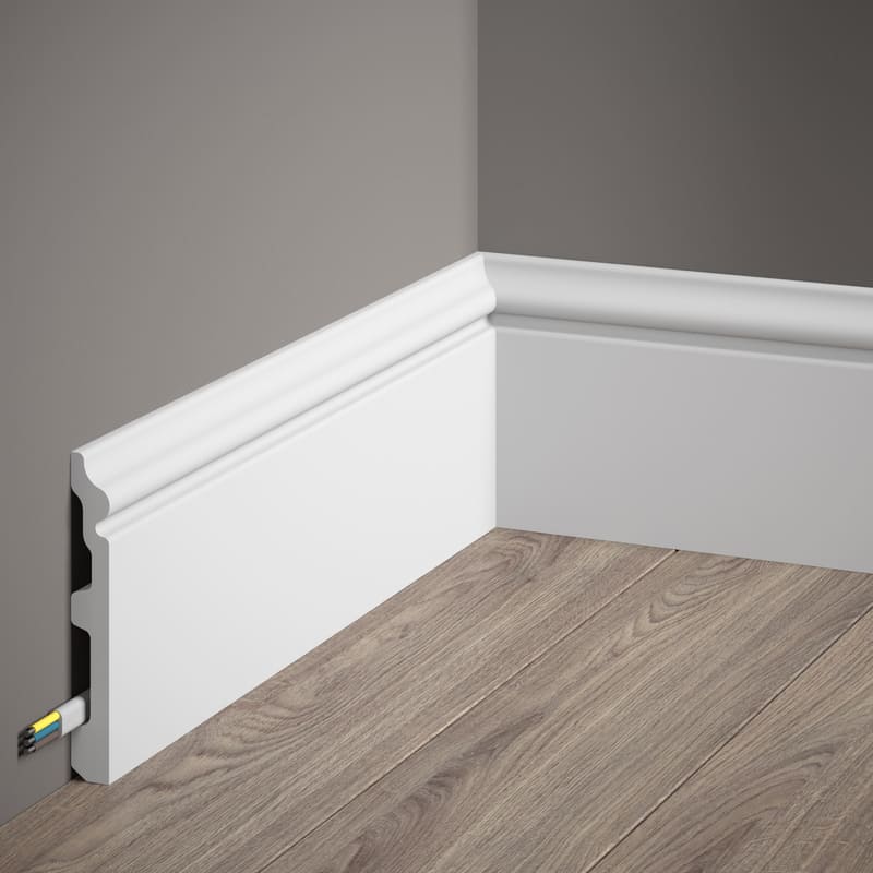 Rodapié blanco decorativo en esquina, instalado sobre suelo de madera, canal para cables