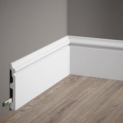 Rodapié blanco decorativo en esquina, instalado sobre suelo de madera, canal para cables
