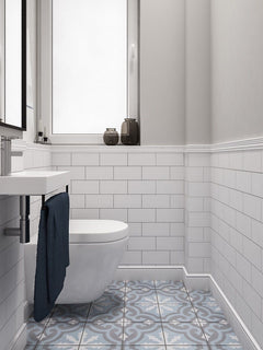 Baño moderno con molduras decorativas blancas, azulejos rectangulares y suelo hidráulico azul gris.