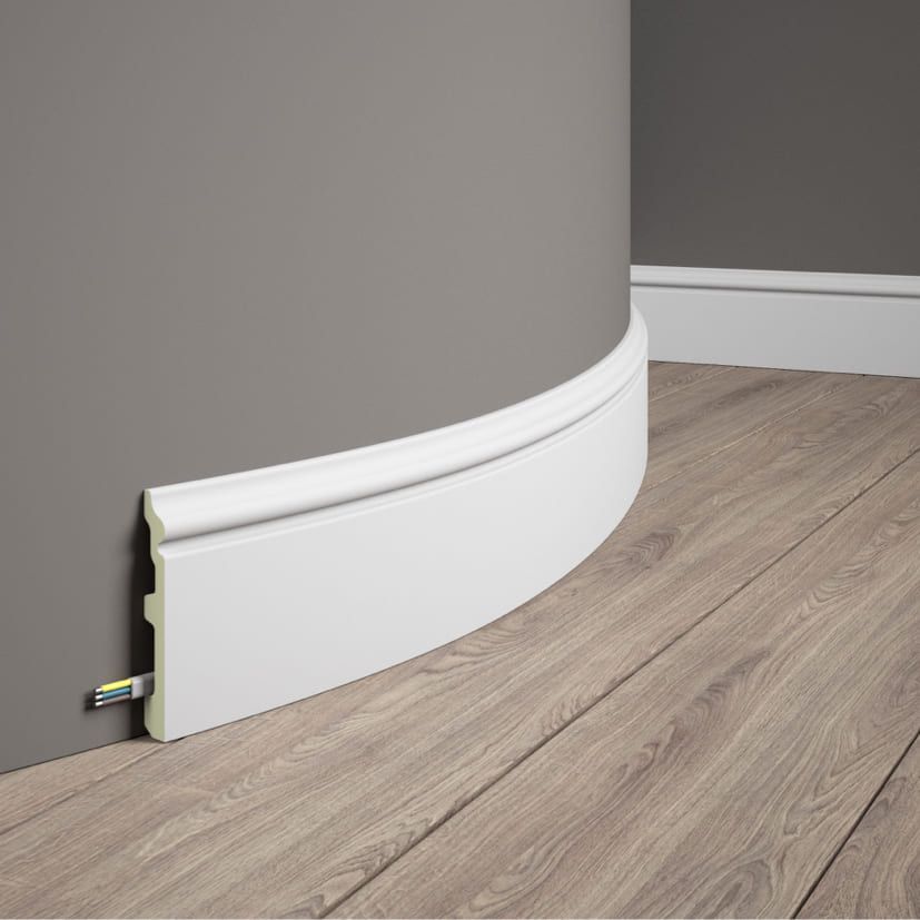 Rodapié flexible blanco para pared curva sobre suelo laminado, con espacio para cables.