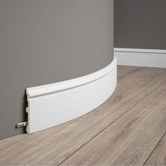 Rodapié flexible blanco para pared curva sobre suelo laminado, con espacio para cables.