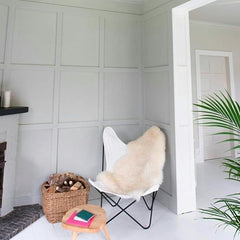 Pared con molduras decorativas grises en sala moderna, silla blanca y cesta de leña