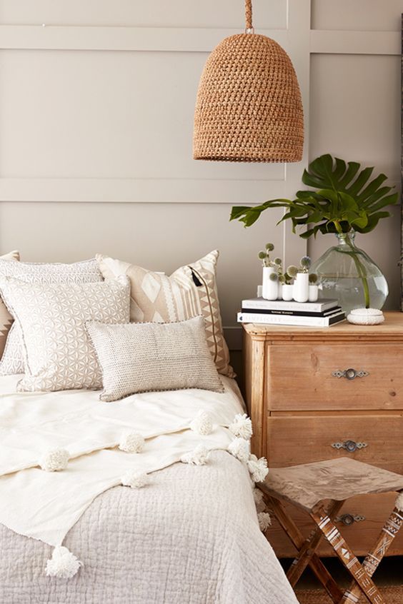Dormitorio con molduras decorativas en pared beige, cama con cojines y mesa de noche de madera.