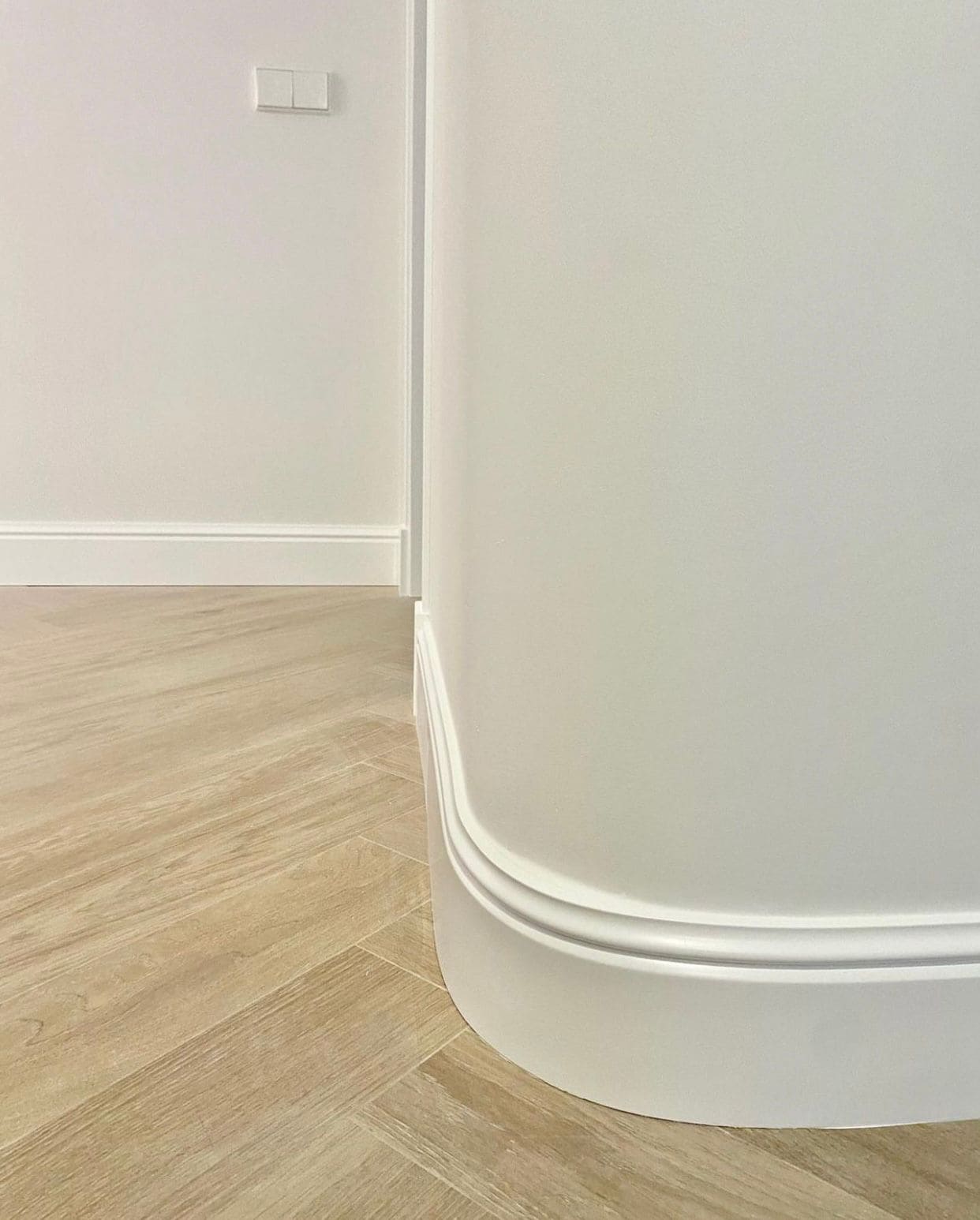 Rodapié blanco curvo en pared blanca con suelo de imitación madera, moldura decorativa