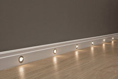 Rodapié blanco decorativo con luces LED integradas sobre suelo de madera clara