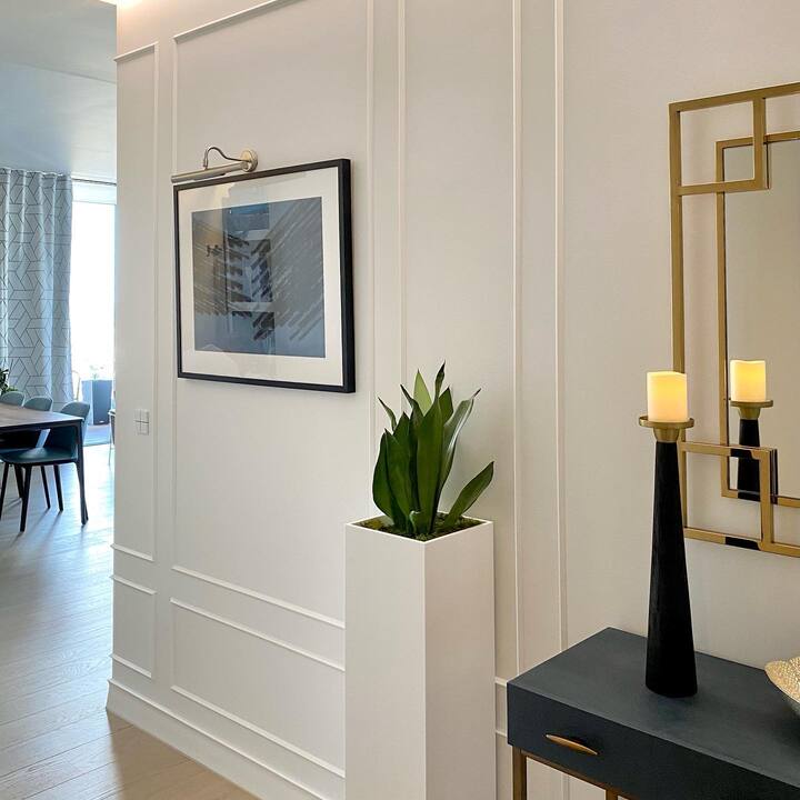 Pared decorada con molduras blancas, cuadro moderno, planta en maceta y consola elegante.