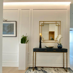 Recibidor moderno con molduras decorativas blancas, consola negra y espejo dorado elegante.