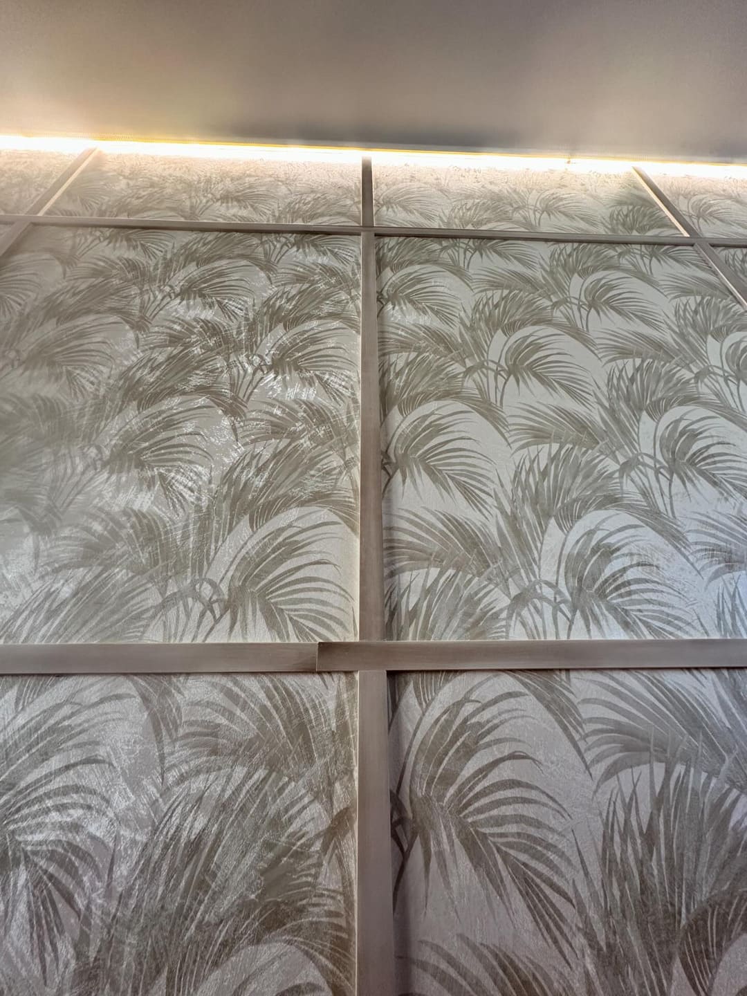Pared decorativa con molduras y papel tapiz de hojas, iluminación LED superior.