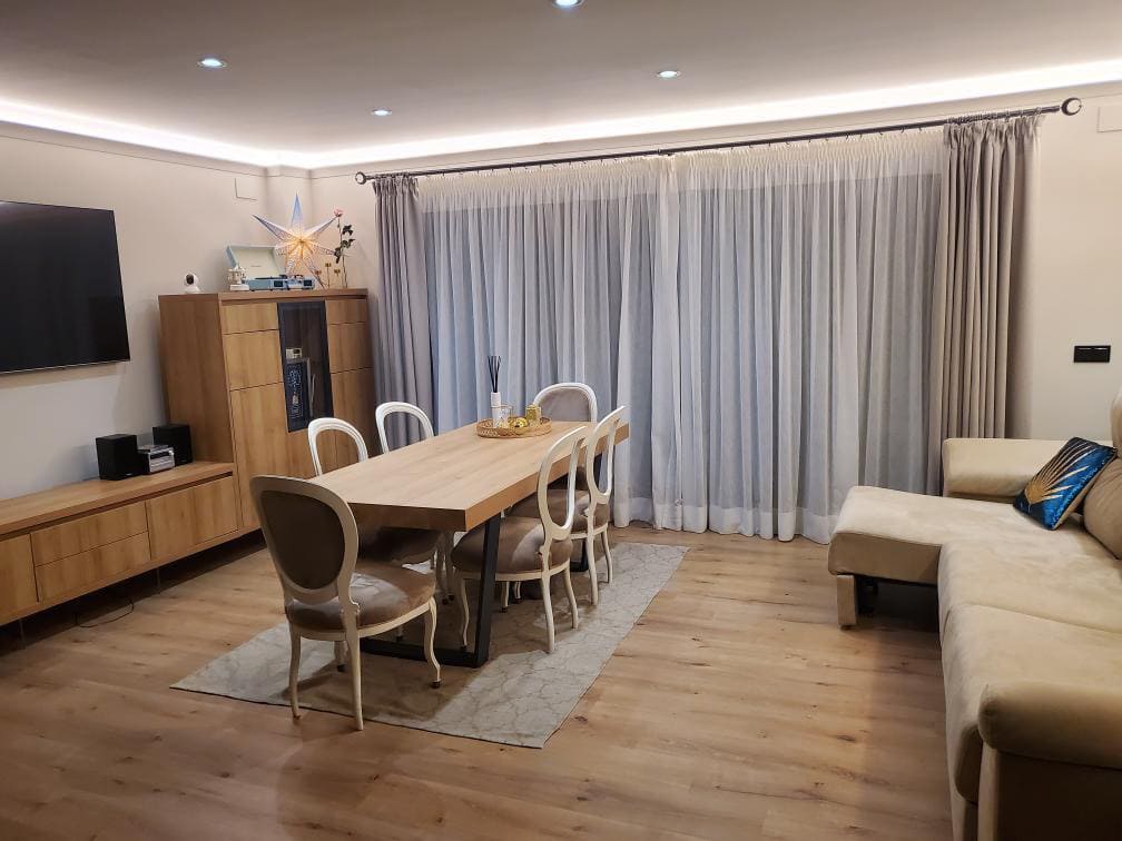 Sala y comedor moderno con piso laminado, molduras decorativas y cortinas elegantes