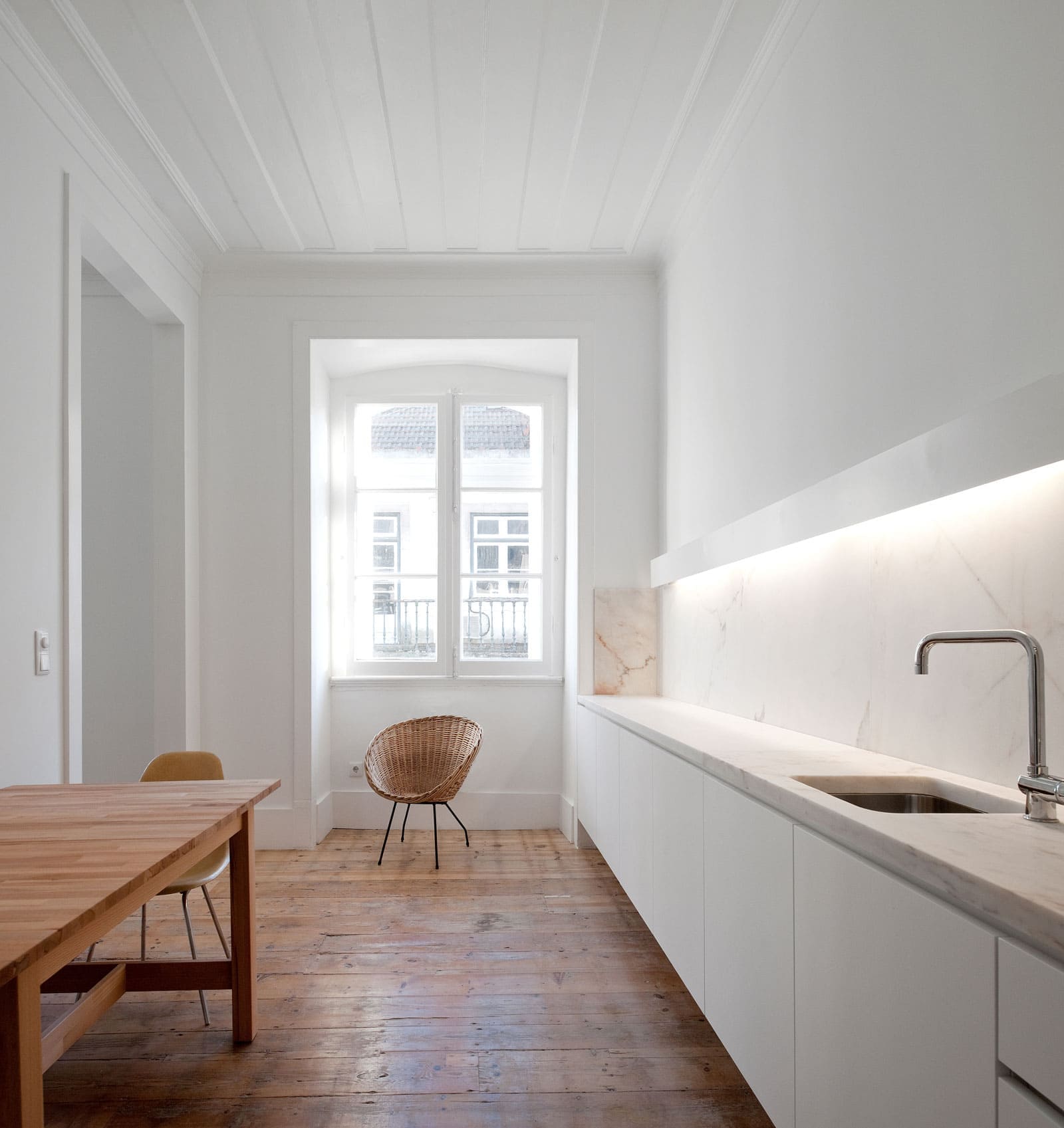 Cocina minimalista con encimera blanca, molduras decorativas y suelo de madera.