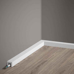 Rodapié blanco moderno para cables en esquina, sobre suelo laminado y pared gris.