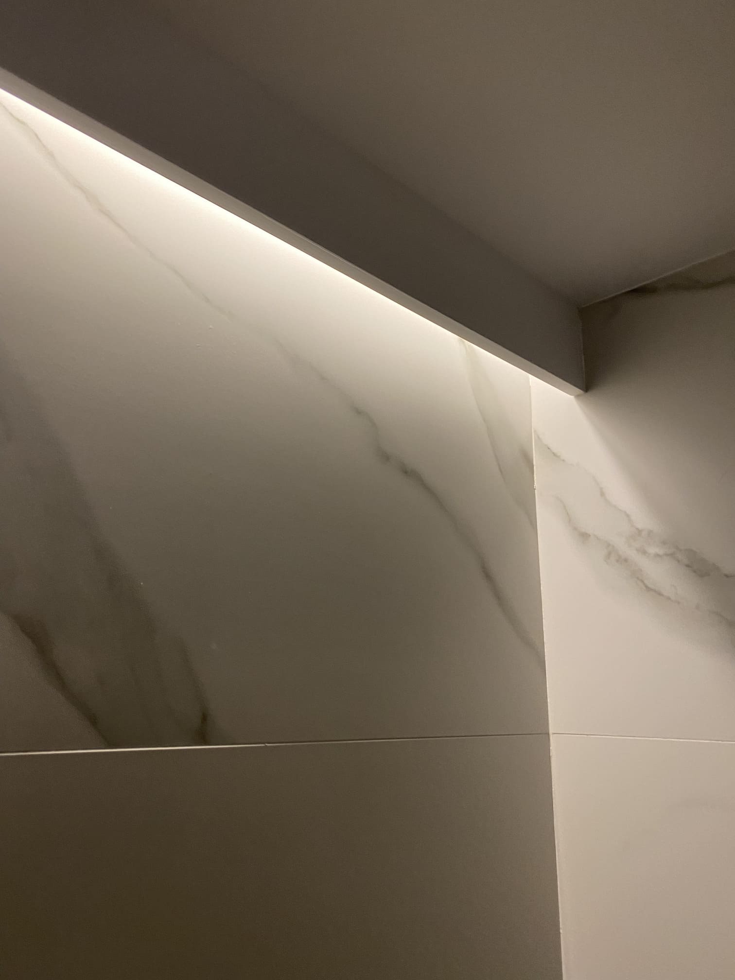 Detalle de moldura decorativa blanca con iluminación LED en pared de baño con acabado mármol.