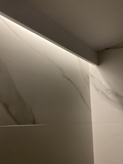 Detalle de moldura decorativa blanca con iluminación LED en pared de baño con acabado mármol.
