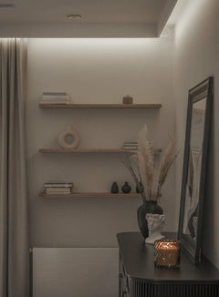 Estante flotante de madera en una pared decorativa con objetos minimalistas y luz ambiental.
