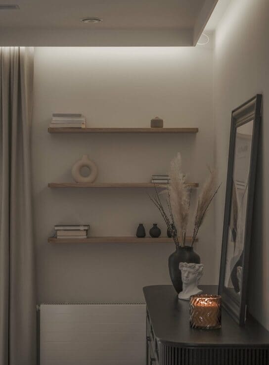 Estante flotante de madera en una pared decorativa con objetos minimalistas y luz ambiental.