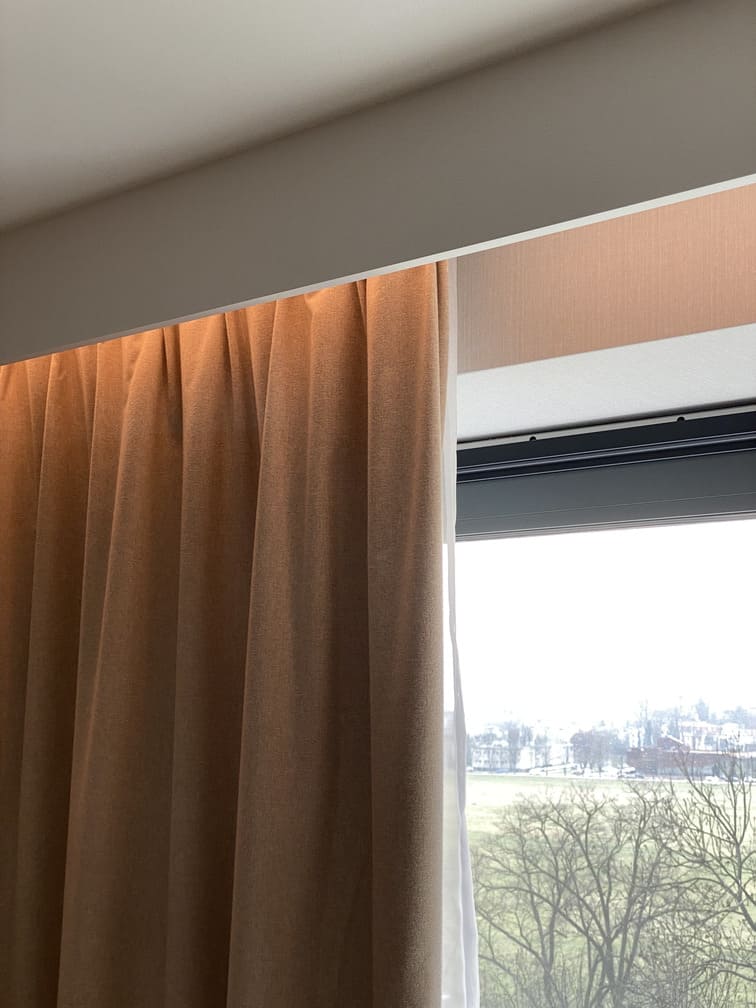 Moldura decorativa de techo blanca instalada sobre cortina en ventana grande con luz natural