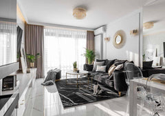Salón moderno con molduras decorativas blancas, sofá gris oscuro, alfombra negra, paredes blancas y detalles dorados.