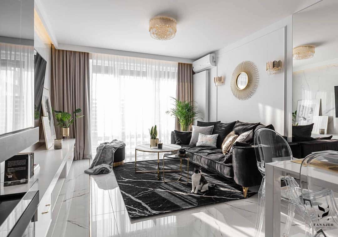 Salón moderno con molduras decorativas blancas, sofá gris oscuro, alfombra negra, paredes blancas y detalles dorados.