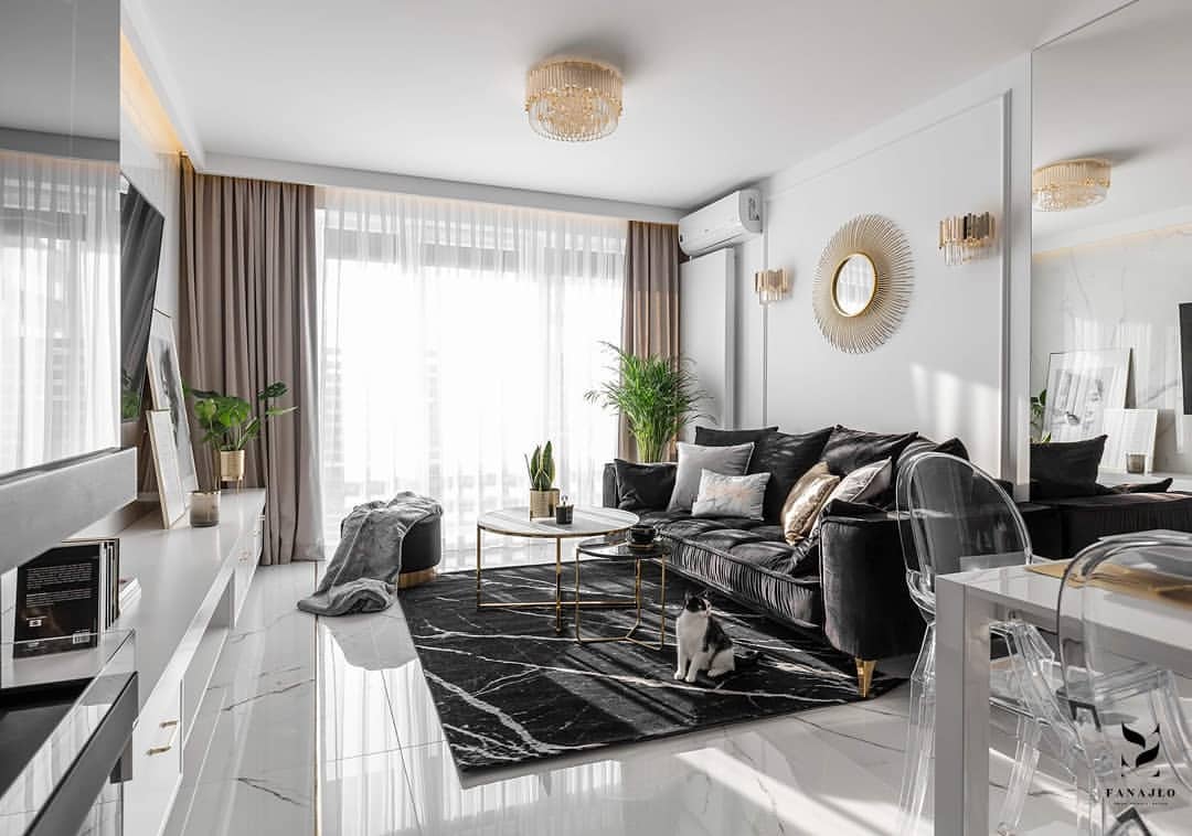 Sala moderna con sofá negro, detalles dorados, molduras decorativas y rodapié blanco.