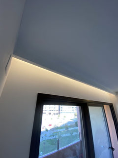Moldura decorativa blanca con iluminación LED sobre ventana en techo inclinado moderno.